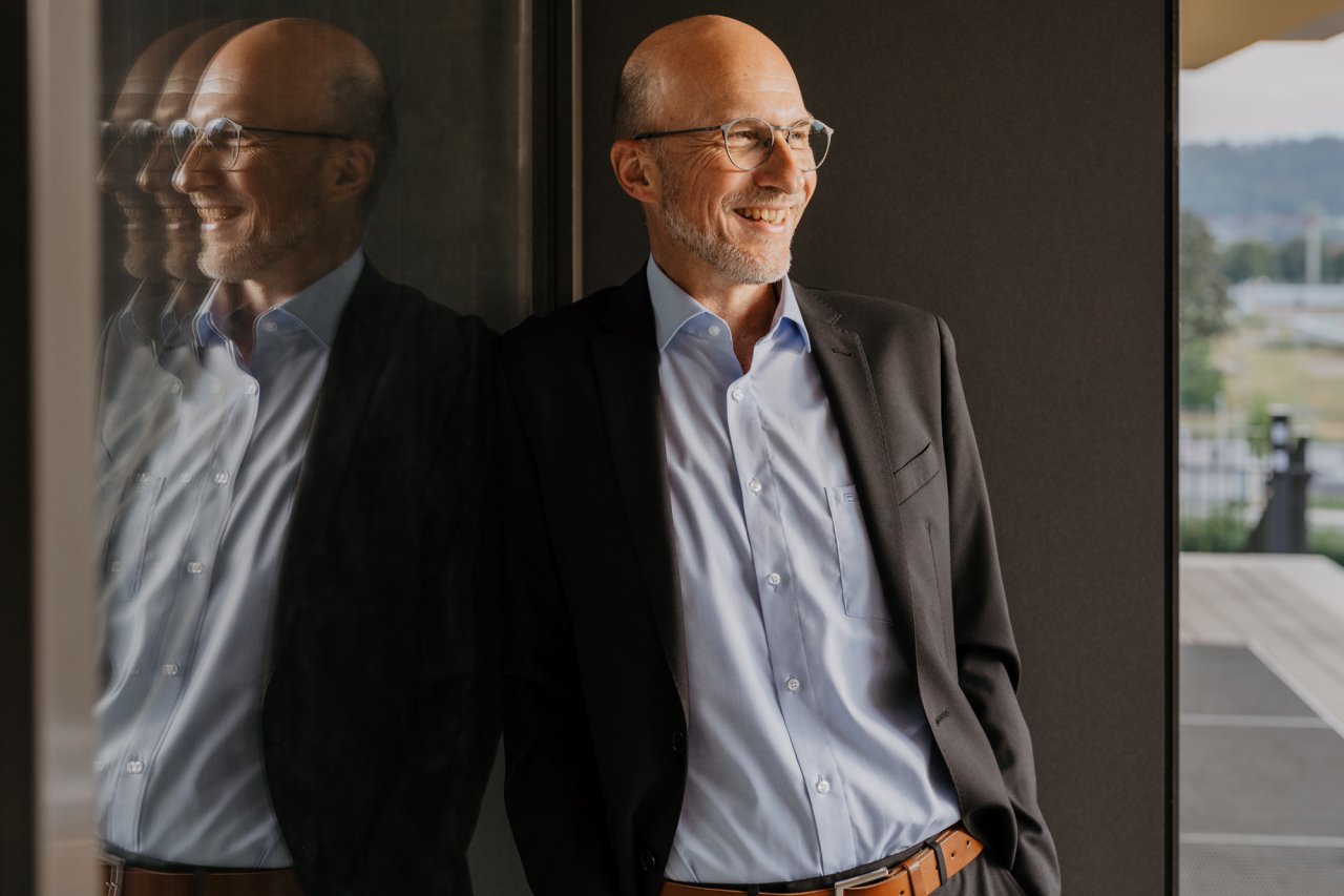 Portraitfoto von Online-Supervisor Jürgen Schuba. Er trägt Sakko und Brille und steht vor einem Gebäude.